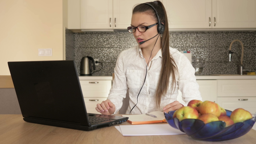 Woman with headset in front of laptop at the table, online consulting. Telework.
