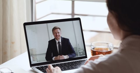 Smiling businessman boss wearing suit making video call conferencing with distance female worker, interviewing job applicant in home office webcam chat meeting on laptop screen. Over shoulder view