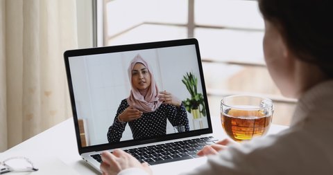 Young indian business woman wears hijab communicates with distance worker in webcam conference chat. Muslim online teacher make video call job interview. Elearning, over shoulder laptop screen view