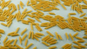 Penne pasta on a light bright blue background. Traditional italian mediterranean food, dry uncooked penne. Dietary nutrition. Slow motion video footage, top view, object movement. Food background.