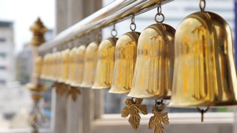 beautiful golden traditional Buddhist bells waved by wind hang on long silver pipe against blurry local buildings closeup