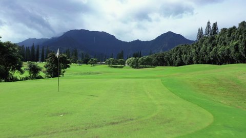 Golf green in Hawaii drone shot low angle close to flag. Mountains in background on sunny day
