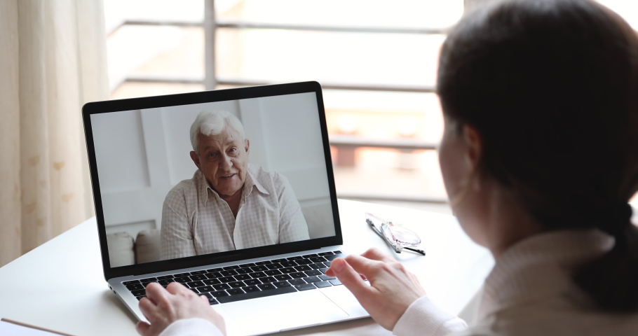 Happy elderly senior father video calling young daughter or doctor by webcam family chat. Grandfather enjoys virtual conversation conference videocall tech app concept. Over shoulder pc screen view Royalty-Free Stock Footage #1050292945