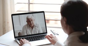 Happy elderly senior father video calling young daughter or doctor by webcam family chat. Grandfather enjoys virtual conversation conference videocall tech app concept. Over shoulder pc screen view