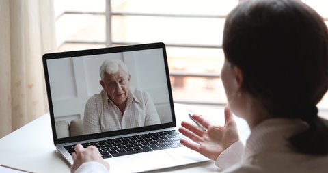 Happy elderly senior father video calling young daughter or doctor by webcam family chat. Grandfather enjoys virtual conversation conference videocall tech app concept. Over shoulder pc screen view