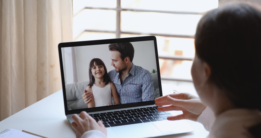 Cheerful husband dad hugging small kid daughter video calling wife mom using computer virtual chat app. Happy family talking on webcam video call concept. Over shoulder closeup laptop screen view Royalty-Free Stock Footage #1050292948