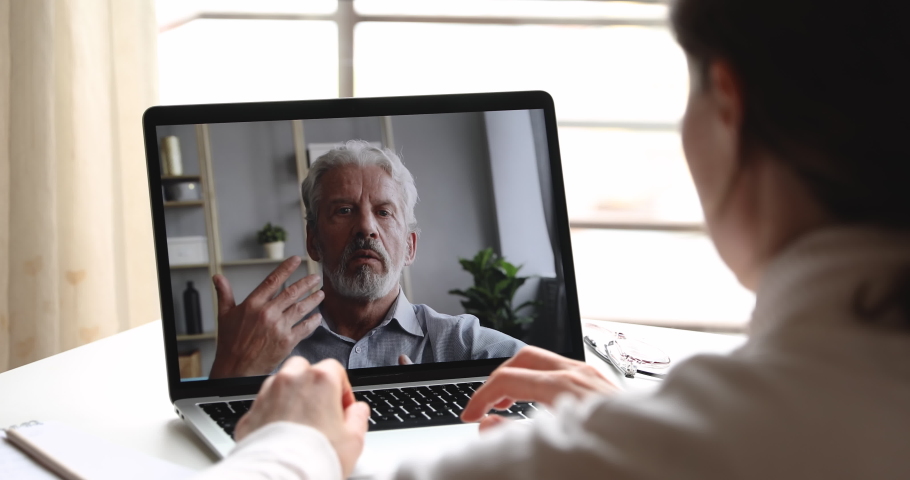 Serious old male online teacher, professional psychologist, coach consulting female student or client via webcam chat video call. Senior father and daughter videocall. Over shoulder laptop screen view | Shutterstock HD Video #1050294226