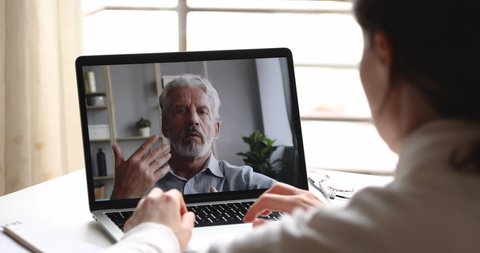 Serious old male online teacher, professional psychologist, coach consulting female student or client via webcam chat video call. Senior father and daughter videocall. Over shoulder laptop screen view