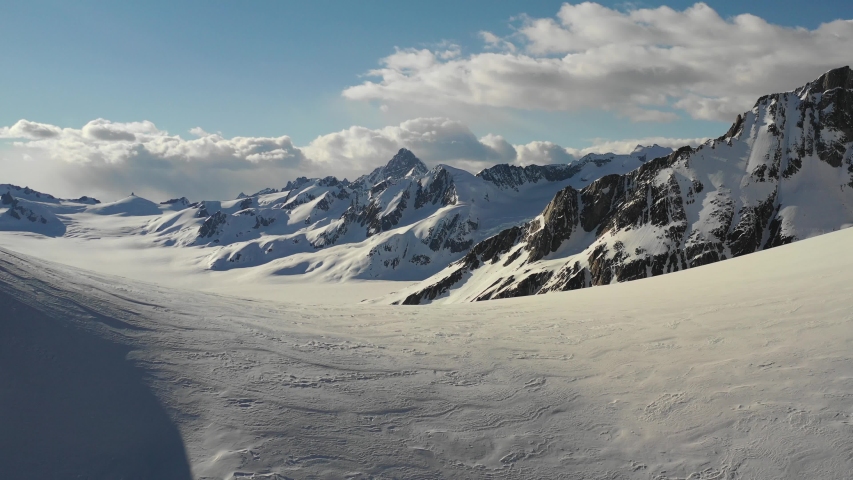 Stunning 4K drone shot flying over snowy saddle to reveal huge mountains on far side Royalty-Free Stock Footage #1050296389