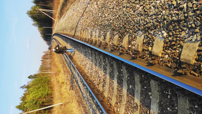 A tired woman in a protective medical mask walks along the railway tracks with a suitcase