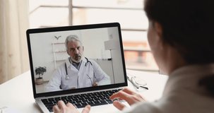 Senior male doctor videoconferencing woman remote patient consulting about corona virus pandemic during telemedicine video call in conference virtual webcam chat app. Over shoulder laptop screen view.
