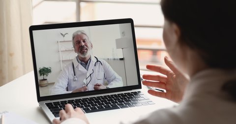 Senior male doctor videoconferencing woman remote patient consulting about corona virus pandemic during telemedicine video call in conference virtual webcam chat app. Over shoulder laptop screen view.