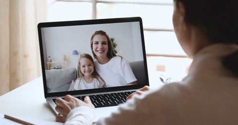 Young woman pediatrician, friend or relative video calling virtual chatting by web cam with happy family cute child daughter and adult mom using tech app on laptop screen. Over shoulder closeup view