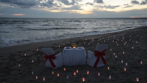 Romantic dinner with candles on sandy sea beach during sunset
