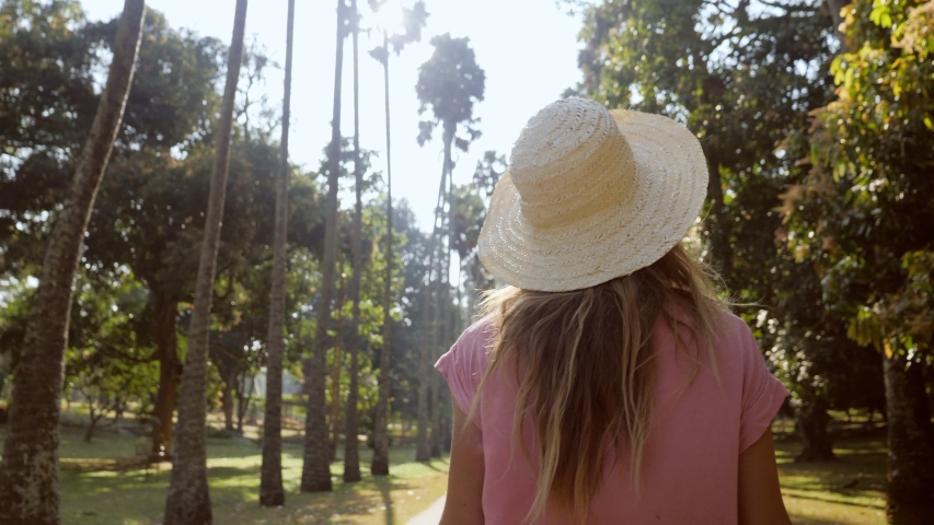Young woman in palm tree avenue spinning around SLOW MOTION. Girl turning around in sunlight happy joy positive emotions concept. People enjoying nature and freedom