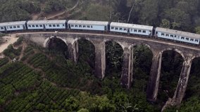 Drone View of the famous blue train passing on nine arch bridge in the jungle in Ella Sri Lanka. Popular and spectacular train ride journey. Aerial view tea plantations 
