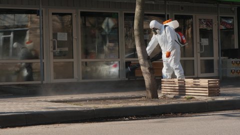 POLTAVA, UKRAINE - CIRCA April 2020: Worker wearing protective clothing for spraying chemicals disinfect the sidewalk and buildings on the street to prevent the spread of the coronavirus