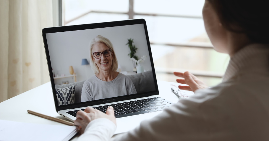 Cheerful older mature woman mother video calling young adult daughter chatting laughing enjoying virtual online conversation talking by webcam wireless app on laptop screen. Over shoulder closeup view Royalty-Free Stock Footage #1050313324