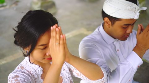 Praying with putting hands to forehead. Young family in Bali pray in temple. Culture and traditions of Indonesia, balinese couple go to temple together for hindu ceremony, rituals. People in Bali