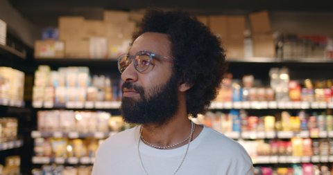 Close up of handsome man in glasses walking and looking around in supermarket. Mature guy in 30s searching for products while doing shopping in grocery store.Blurred background.