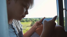 Closeup view video portrait of cute white young teenage kid sitting alone on windowsill of window in countryside cottage playing online video games using modern mobile smartphone.