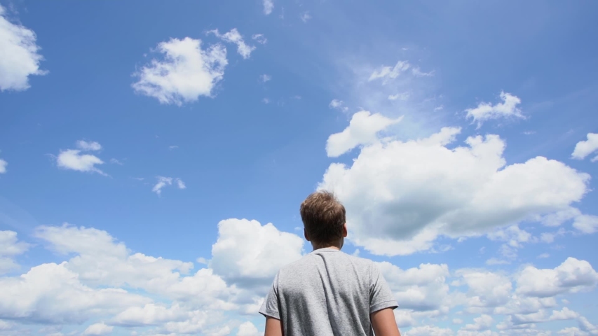 Close up back view of one white caucasian young kid standing alone outdoors isolated at bright sunny blue sky background. Boy looking forward.