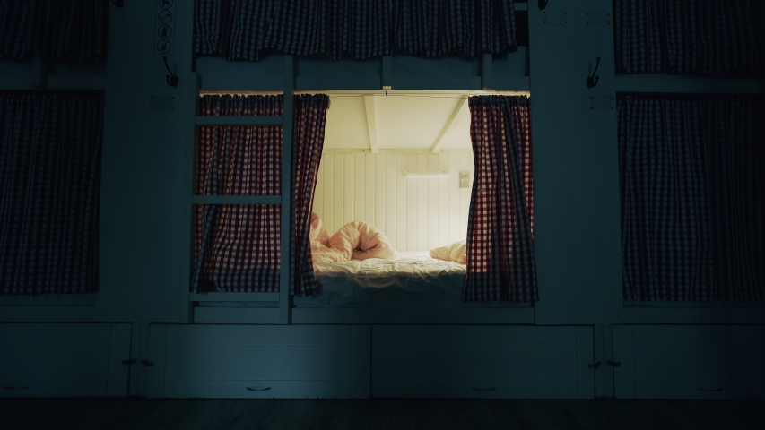 Young girl lays down in bed and falls asleep in cozy hostel room