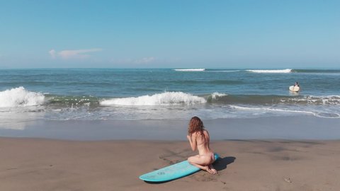 Aerial view of beautiful sporty surfing woman in sexy bikini sit near longboard surf surfboard board on beach before surfing. Modern active sport lifestyle and summer vacation.