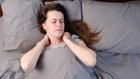 Top close up view upset young woman lying in bed in morning feels pain in neck after night sleep, awaken having painful sudden ache or stiffness, incorrect posture during sleep. Fibromyalgia concept