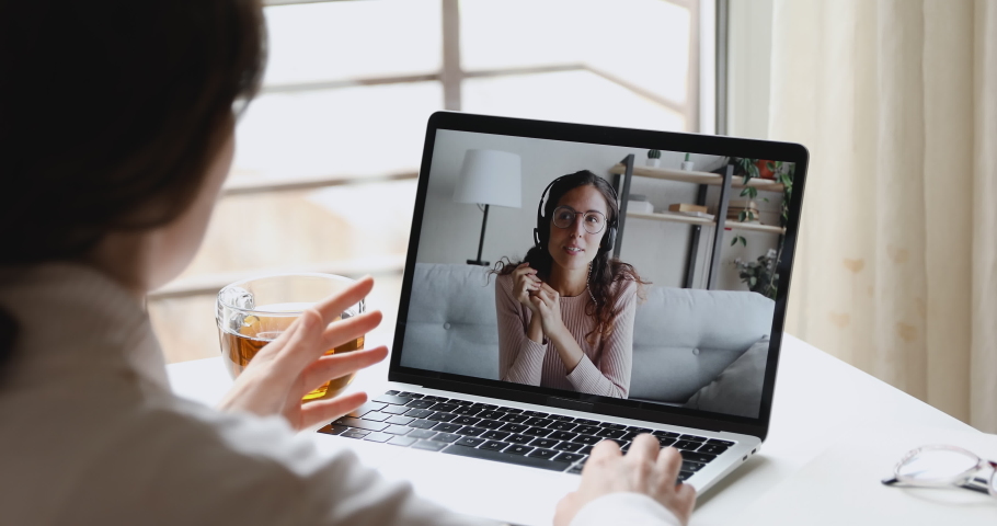 Happy young online teacher wears headset communicates with distant student gives web education class talks in webcam chat video conference call on laptop screen. Elearning concept. Over shoulder view | Shutterstock HD Video #1050346030
