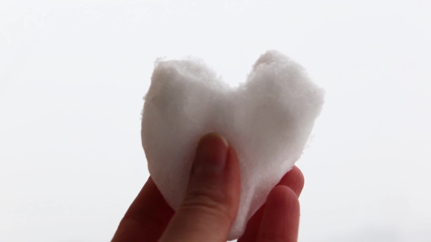 Hand holding heart made of snow with snowflakes falling on the background