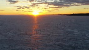 Aerial video view of backwards flying over ice of frozen Ob sea at amazing sunset with yellow Sun and red clouds