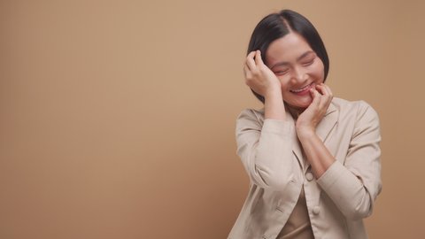 Happy asian business woman feel shy standing with copy space isolated over beige background. 4K video