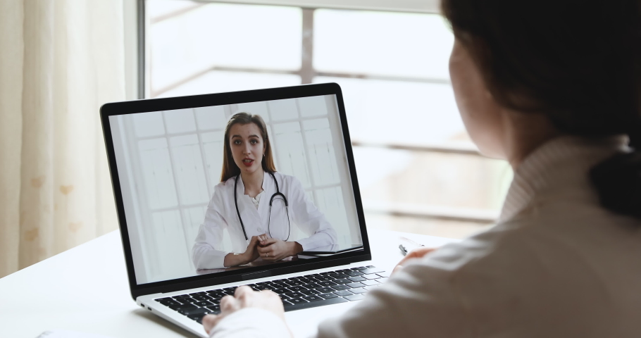 Young woman patient talking with online female doctor therapist in webcam video call app on laptop screen. Remote telemedicine healthcare medical consultation concept. Over shoulder close up view Royalty-Free Stock Footage #1050355294