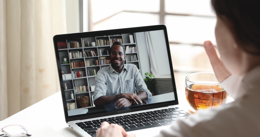Friendly african male online teacher, distance tutor or manager talking with female remote employee, student, client by web cam video call conference chat on laptop screen. Over shoulder closeup view Royalty-Free Stock Footage #1050356800