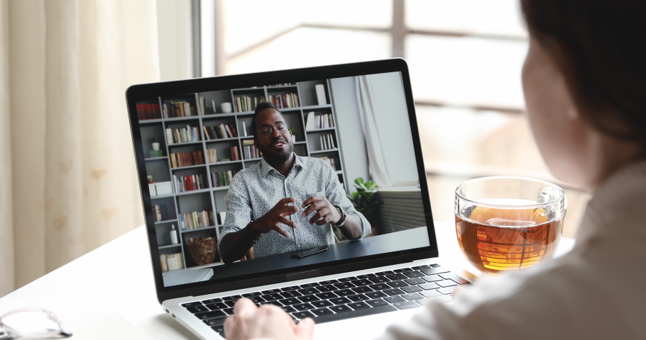 Friendly african male online teacher, distance tutor or manager talking with female remote employee, student, client by web cam video call conference chat on laptop screen. Over shoulder closeup view | Shutterstock HD Video #1050356800
