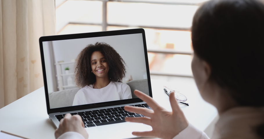 Over shoulder view of caucasian online teacher, remote tutor or psychologist conferencing with african school girl student on distance learning video call at home. Online study by webcam chat concept Royalty-Free Stock Footage #1050359014