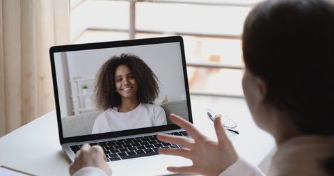 Over shoulder view of caucasian online teacher, remote tutor or psychologist conferencing with african school girl student on distance learning video call at home. Online study by webcam chat concept