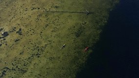Aerial footage of two persons in each their kayak paddling over the sea, on a beautiful sunny day. One red and one yellow kayak. The sea goes from very shallow to very deep in right side of the frame.