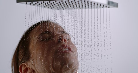young woman taking a shower in slow motion. beautiful girl head under the shower enjoying the drops and the water flow on her face
