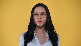 Shocked businesswoman in eyeglasses looking at camera isolated on yellow