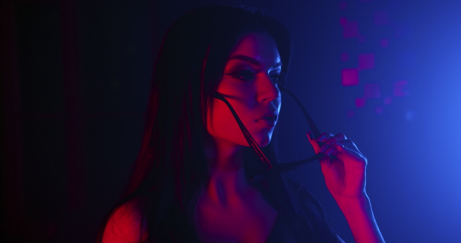 The girl is slowly and sexually putting on her glasses. Shooting in blue and red neon. 4k