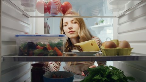 Beautiful Young Woman Opens Refrigerator Full of Organic Food and Grabs a Green Prepared Salad in a Plastic Reusable Box. Diet and Healthy Way of Life Concept. POV From Inside the Fridge.