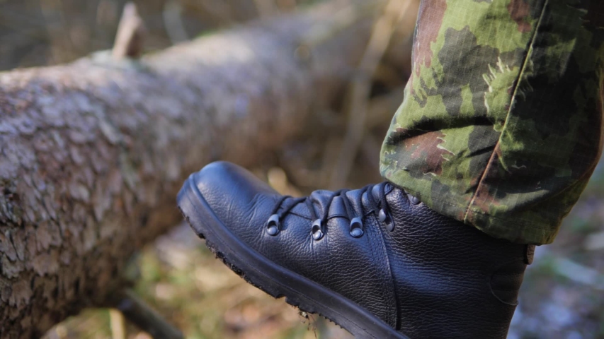 A person wearing camouflage military trousers and a thick leather boot kicking a fallen tree log and spraying mud Royalty-Free Stock Footage #1050392452