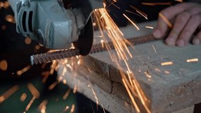 A man holds an angle grinder in his hands and cuts off a metal rod with it. Slow motion video.