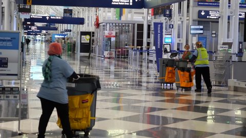 Chicago, IL / USA - April 10 2020: three airport cleaners push their supplies down an empty corridor at O'Hare International Airport during the COVID-19 pandemic