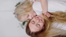 Vertical format video of happy blond little girl hugging and kissing her cheerful mother