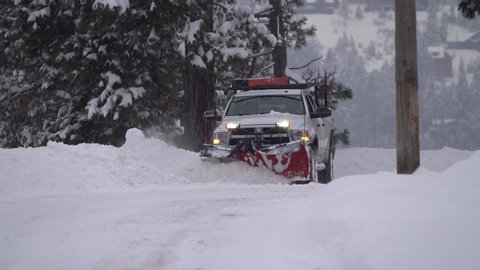 Slow motion clip of a pickup truck plowing snow with a red snow plow while snowing.