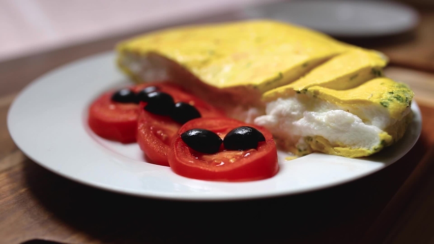 Omelet eating. The view of cutting an omelet and eating with a fork and knife. Traditional morning breakfast service.