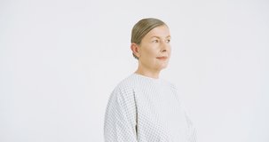 Portrait of ill middle-aged Caucasian woman with coronavirus in hospital outfit on white wall background with slight smile. Medical female patient in nice mood. Close up. Disease concept.